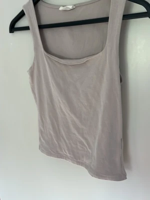 Beige ärmlös linnetopp - Snygg beige linnetopp med breda axelband och rundad halsringning. Toppen är enkel och stilren, perfekt att matcha med jeans eller kjol. Tillverkad i mjukt material som känns skönt mot huden.