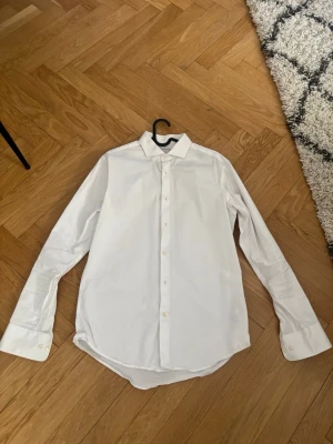 Vit skjorta från Tiger of Sweden - Klassisk vit skjorta från Tiger of Sweden i slim fit. Skjortan har långa ärmar, knappar framtill och en stilren krage. Perfekt för dig som gillar en clean och tidlös look. Materialet är mjukt och känns skönt mot huden.