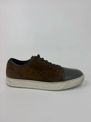 Bruna Lanvin sneakers med lackad tå - Snygga bruna sneakers med ovandel i mocka och en glansig, mörkgrå lackad tå. Skorna har vita sulor och bruna skosnören. Perfekt för dig som gillar en stilren men ändå unik look.