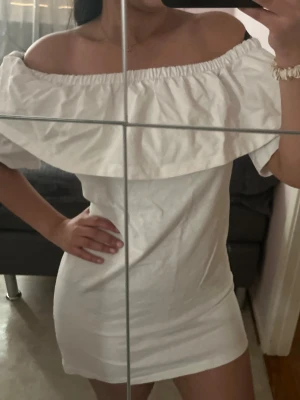 Vit offshoulder kortklänning - Säljer en söt vit kortklänning med offshoulder-design och bred volang runt axlarna. 