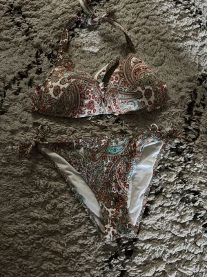 Mönstrad calzedonia bikini  - Snygg bikini med paisleymönster i brunt, grönt och vitt. Överdelen har halterneck med knyt och en liten cut-out framtill. Underdelen har knyt i sidorna för justerbar passform och aldrig använd. Perfekt för stranden eller poolen!