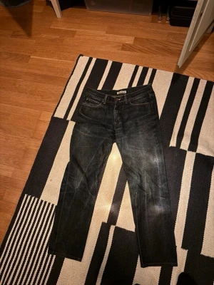 Mörkblå raka jeans från Nudie - Snygga mörkblå jeans från Nudie med klassisk femficksdesign och raka ben. Jeansen har subtila slitningar och kontrastsömmar, vilket ger en cool och avslappnad look. Perfekta för dig som gillar stilrena och tidlösa jeans i denim.