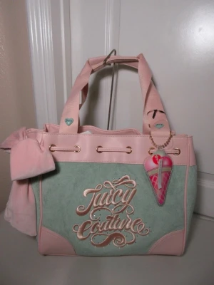 Juicy Couture daydreamer tote pastellgrön - Superfin handväska från Juicy Couture i pastellgrönt och ljusrosa med broderad logga framtill. Väskan har detaljer i guld, ett stort rosettband på sidan och ett hjärtformat hänge. Materialet är en mix av mocka och konstläder.