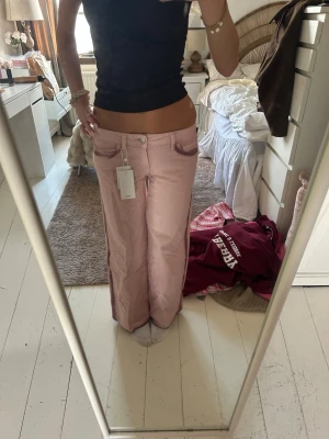 Vida rosa jeans från Mango - Säljer ett par ljusrosa jeans från Mango med breda ben och hög midja. Klassisk femficksmodell med knapp och dragkedja framtill. Jeansen har en trendig loose fit och är tillverkade i ett mjukt denimtyg. Perfekta för dig som vill ha en cool och avslappnad look.