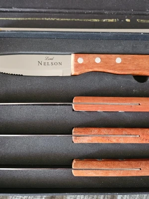 Lord Nelson knivset med trähandtag - Säljer ett knivset från Lord Nelson med blad i rostfritt stål och handtag i trä med metallnitar. Setet innehåller flera knivar med tandad egg, perfekt för köket. Levereras i en svart presentförpackning med text från Lord Nelson. Aldrig använda, förpackningen har gått sönder efter öppnande.