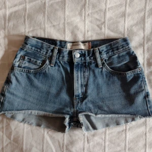 Levis 505 blå jeansshorts - vintage cut off shorts  - Skitsnygga blå avklippta jeans 505 från Levis. Klassisk femficksdesign, råa kanter nertill och Levi's-patch bak. Perfekta för sommaren med sin avslappnade vibe och snygga passform. Bälteshällor och knappgylf. Ikonisk denimstil som aldrig går ur tiden. Storlek midja: 29.