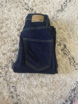 Mörkblå utsvängda jeans 157 - Snygga mörkblå jeans från 157 med utsvängda ben och klassiska kontrastsömmar. Jeansen har fem fickor och hög midja, perfekta för en trendig och avslappnad look. Materialet är denim i bomull.