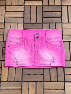 Rosa jeanskjol med slitningar - Cool rosa kort jeanskjol med slitna detaljer framtill och dubbla knappar i midjan. Kjolen har klassiska fickor både fram och bak och är perfekt för dig som vill sticka ut med färg. Snygg att matcha med en enkel topp eller hoodie. Midjemått 39-41 stretchig!❣️❣️