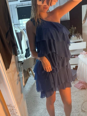 Blå one shoulder volangklänning - Snygg blå kortklänning med flera lager volanger och one shoulder-design. Klänningen har en luftig och lätt känsla, perfekt för dig som vill sticka ut. Passar dig som gillar trendiga och unika plagg. Jag har vanligtvis storlek s men denna är storlek 42. 