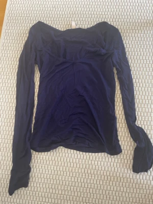 Mörkblå långärmad topp med spetskant - Mörkblå långärmad topp med fin spetskant runt halsringningen. Toppen har en smickrande passform och är tillverkad i mjukt material som känns skönt mot huden. Perfekt att styla med jeans eller kjol för en trendig look.