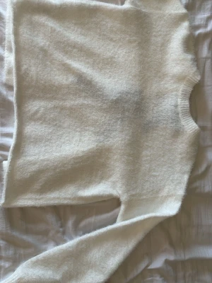 Vit fluffig kofta med svarta rosetter - Supersöt vit fluffig kofta med två svarta rosetter som knytning framtill. Koftan har lång ärm och är gjord i ett mjukt, lurvigt material som känns riktigt cozy. Perfekt för dig som gillar en söt och trendig look.