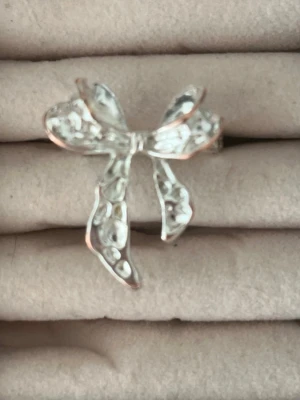 Söt silverfärgad rosettring - Säljer min fina ring i form av en rosett med hamrad yta i silverfärg. Ringen har trendig design som sticker ut och passar perfekt för dig som gillar detaljer. Den har tappat lite av sin färg men det är inget som syns när den är på