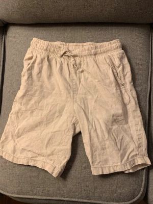 Beige linneshorts med snörning - Snygga beige shorts i linne med elastisk midja och snörning framtill. Shortsen har sidofickor och en bakficka, perfekt för chill dagar. Lätta och luftiga, perfekta för varma sommardagar.