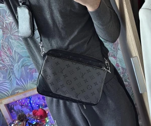 Svart axelväska Louis Vuitton monogram - Snygg svart axelväska från Louis Vuitton med klassiskt monogrammönster i grått. Väskan har en rektangulär form, justerbar axelrem och en mindre avtagbar ficka. Tillverkad i canvas med detaljer i läder och metallspännen.