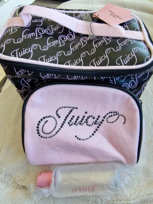 Juicy Couture necessärset rosa & svart - Necessärset från Juicy Couture med en större svart väska med vitt logomönster och rosa detaljer samt en mindre rosa necessär med strasslogga. Medföljer även en liten flaska med rosa lock. Perfekt för smink eller reseprodukter.