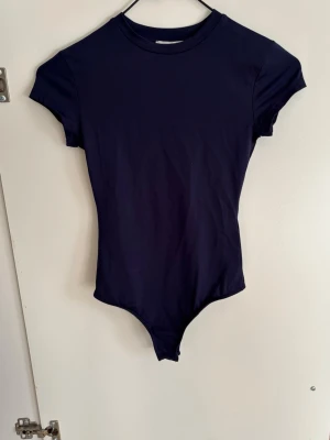 Mörkblå kortärmad body - En stilren mörkblå body med korta ärmar och rund halsringning. Perfekt att matcha med jeans eller kjol för en enkel och snygg look. Tillverkad i ett mjukt och stretchigt material som sitter skönt mot kroppen.