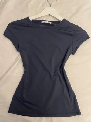 Mörkblå tight t-shirt från Zara - Snygg mörkblå t-shirt från Zara i en tight passform. T-shirten har korta ärmar och rund halsringning. Perfekt basplagg i mjukt och stretchigt material som sitter skönt på kroppen.