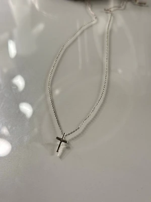 Silverhalsband med korsberlock - Stilrent halsband i silver med en enkel korsberlock. Kedjan är tunn och smidig, perfekt för att ge en minimalistisk touch till din outfit. Säljer denna endast för att jag bytt från silver till guld, hade denna på mig konstant, den är silverdoppad. Fick denna som present så minns tyvärr inte vart mina vänner köpte den ifrån. 