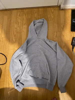 Grå basic hoodie med magficka - Enkel och stilren grå hoodie med huva och stor magficka framtill. Hoodien har ribbade muddar vid ärmslut och nederkant. Perfekt för en avslappnad och bekväm stil. Materialet är mjukt och känns skönt mot huden.