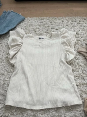 Vit ribbad topp med puffärmar - Trendig vit topp med ribbad struktur och stora puffärmar. Rund halsringning och loose fit ger en avslappnad men stylish look. Perfekt att matcha med jeans eller kjol för en cool vibe.