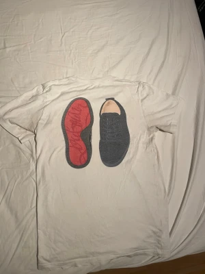 Vit t-shirt med sko-tryck - Säljer min loubistin tröja, bra passform, skicket är bra.