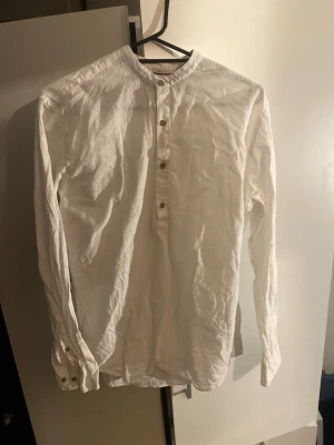 Vit henley-tröja i linne från Jack and Jones premium - Vit långärmad henley-tröja från Jack and Jones med knappar framtill och klassisk krage. Skjortan är tillverkad i linne och har en avslappnad passform. Perfekt för en stilren och enkel look i sommar. Aldrig använt!