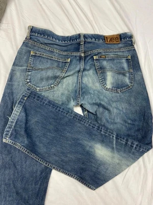 Blå Lee jeans med raka ben - Snygga blå jeans från Lee med raka ben och klassisk femficksdesign. Jeansen har slitna detaljer och ljusare partier för en cool vintagekänsla. Tillverkade i denim med Lee-logga på bakfickan. Perfekta för en avslappnad streetstil.