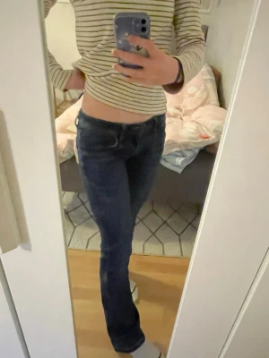 Mörkblå bootcut jeans - Säljer ett par mörkblå bootcut jeans med klassisk femficksdesign och låg midja. Jeansen har en snygg passform som sitter tajt över låren och släpper ut vid vaden. Perfekta till sneakers eller boots.