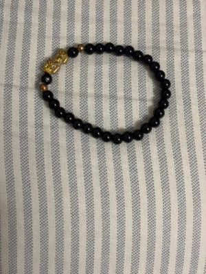 Svart pärlarmband med gulddetalj - Snyggt armband med svarta runda pärlor och små guldfärgade detaljer. Armbandet har en dekorativ guldfärgad lejonfigur som ger en cool touch. Perfekt accessoar för att lyfta din stil.