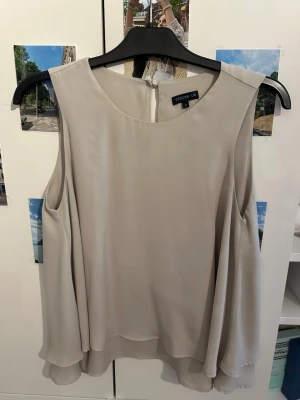 Beige ärmlös blus från STOCKH LM - Snygg beige blus från STOCKH LM med dubbla lager och rund halsringning. Modellen är ärmlös och har en lätt, flowy passform med knytning i nacken. Perfekt för en stilren look.