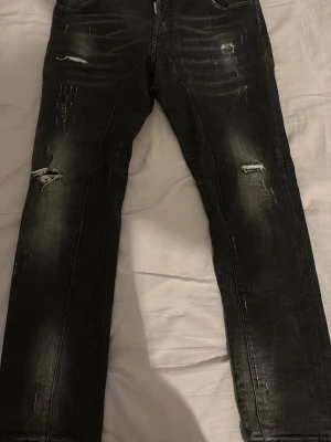 Svarta slitna jeans från Dsquared2 - Säljer ett par svarta jeans från Dsquared2 med snygga slitningar och distressed detaljer. Jeansen har smal passform och klassisk femficksdesign. Perfekta för dig som gillar en edgy och trendig stil.