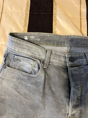 Gråa straight tapered jeans G-Star - Snygga gråa jeans från G-Star RAW, modell 3301 Straight Tapered. Klassisk femficksdesign med dragkedjegylf och bälteshällor. Jeansen har en tvättad look och är tillverkade i bomullsdenim för en bekväm känsla.