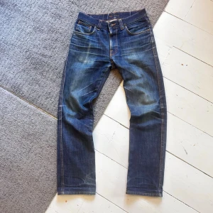 Mörkblåa Nudie Dry Slim Jim Jeans - Sjukt feta Nudie jeans med starka fades. | W30 L32. | Väldigt fint skick, förutom en minimal fläck som knappast syns (Se bild). | Midja: 39cm, Längd: 101cm. | Skriv vid minsta fundering, pris ej hugget i sten. 