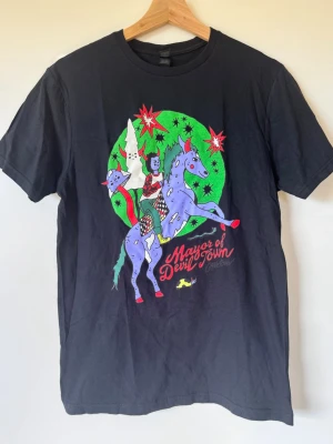 Cavetown Merch Svart t-shirt Mayor of Devil Town  - Merch från artisten Cavetown. Aldrig använd T-shirt med färgglatt tryck av en tecknad figur på en lila häst och texten 'Mayor of Devil Town'. Motivet har starka färger som grönt, rött och lila, och t-shirten har en klassisk passform med rund/hög hals och korta ärmar. Den är köpt från Cavetowns merch hemsida. Storlek S! 100% bomull. 