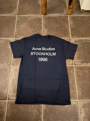 Acne studios t shirt  - Riktigt fet och eftertraktad t-shirt med acne studios loggan i storlek S. Väldigt bra skick!  Obs: Jag är lite osäker på äktheten då lappen i nacken saknas, därför säljs den billigare (499 kr, nypris ca 3000 kr). längd cirka 65cm, bredd cirka 44cm. Tveka inte att höra av dig vid frågor eller funderingar!