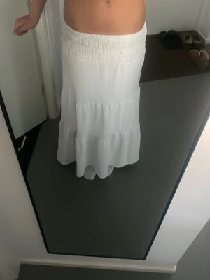 Vit långkjol med volang - Säljer en super snygg vit långkjol med bred resår i midjan och volangdetaljer. Kjolen är luftig och super skön, perfekt för varma dagar. Enkel att matcha med crop tops eller linnen. Passar värnplikten till ALLT 