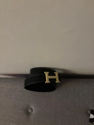H bälte, Svart skärp med guldfärgat H-spänne - Snyggt bälte med ett h spänne i guld, ingen box till bältet finns tyvärr inte. Det är 125cm bälte. Skriv t mig vid frågor. Ingen box