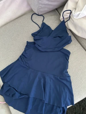 Mörkblå bikini med volangdetaljer - Snygg mörkblå top å kjol  med volangdetaljer och smala axelband. Toppen har omlott-look och kjoldel med volanger för en trendig och feminin stil. Perfekt för strandhäng eller poolparty.