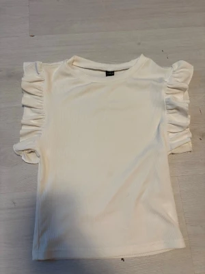 Topp shein   - Superfin vit ribbad topp från SHEIN med korta volangärmar. Toppen har en rund halsringning och är tillverkad i ett stretchigt material som sitter snyggt. Perfekt att styla med jeans eller kjol för en trendig look.tveka inte att höra av er vid frågor eller funderingar😇💕