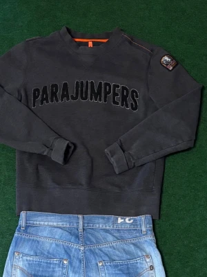 Parajumper tjocktröja  -  Det Parajumpers sweatshirt i storlek S (PASSAR M!) Säljer en äkta Parajumpers tjocktröja i mycket fint skick. Stilren mörkgrå modell med broderad “PARAJUMPERS”-logga framtill och klassisk patch på ärmen. Väldigt skön och kvalitativ sweatshirt med premiumkänsla.  📏 Storlek: S, men passar som M  ✨ Skick: Jättebra skick utan större anmärkningar. ✅ 100% äkta.  BUDA !