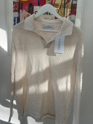 Beige stickad tröja från Ciszere - Snygg beige stickad tröja från Ciszere med krage och lång ärm. Tröjan har ett diskret mönster i stickningen och är perfekt för dig som gillar en stilren och avslappnad look. Storlek L men ganska liten i storleken, passar även M.