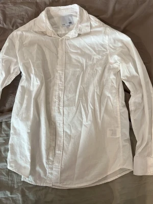 Vit skjorta från 157 i bomull - Klassisk vit skjorta från 157 i storlek M. Skjortan har lång ärm, knappar framtill och är tillverkad i mjuk bomull. Perfekt för en clean och stilren look.