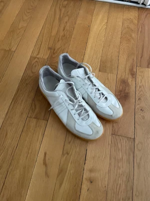 Vintage gats - Snygga vita sneakers med beige mockadetaljer och klassisk gummisula. Skorna har lågt skaft, vita skosnören och stilrena paneler i både läder och mocka. Perfekta för en clean och tidlös look.
