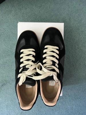 Svarta sneakers Maison Margiela - Svarta sneakers från Maison Margiela med ovandel i mocka och läder, vita snören och beige innersula. Box medföljer 