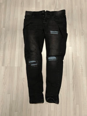 Svarta slitna skinny jeans 32EU - Svarta skinny jeans med slitningar och lagade detaljer på låren och knäna. Jeansen har klassisk femficksdesign och knappgylf. Materialet är denim med stretch för en bekväm passform. Perfekta för en trendig och avslappnad stil.