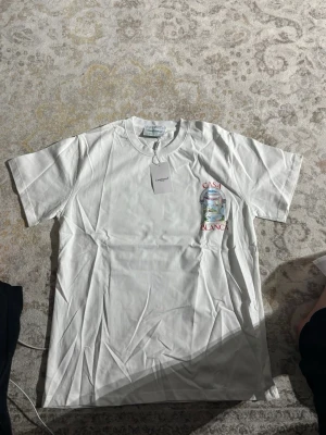 Vit Casablanca t-shirt med tryck - Snygg vit t-shirt från Casablanca med färgglatt tryck av ett fönster och texten 'CASA BLANCA' både fram och bak. T-shirten har rund hals och är tillverkad i mjuk bomull. Perfekt för dig som gillar stilrena plagg med unik design.