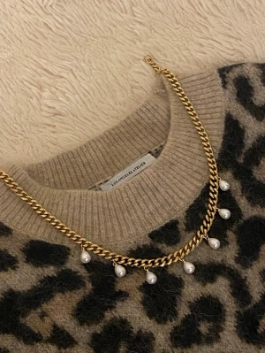 Guldfärgat halsband med pärlor - Snyggt halsband i guldfärgad rostfritt med kedja och hängande vita pärlor. Perfekt för att ge outfiten en trendig och elegant touch. Kedjan har en klassisk design och pärlorna ger en extra detalj som sticker ut.