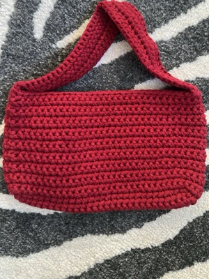 Handvirkad röd väska - Unik handvirkad axelväska i djup röd färg. Väskan 29x17 cm bred med axelrem på 45x4,5cm.Gjord i tjockt garn som ger chunky look.