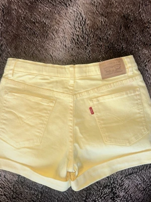 Gula shorts från Levi's - Snygga ljusgula shorts från Levi's med klassisk femficksdesign och uppvikta benslut. Shortsen har bälteshällor, knapp och dragkedja framtill samt Levi's ikoniska läderpatch bak. Perfekta för varma dagar!