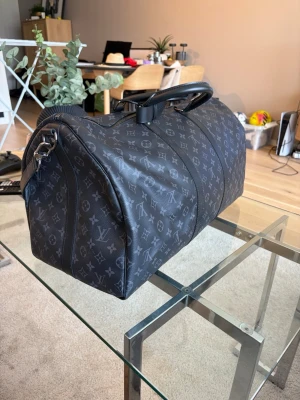 Louis Vuitton svart monogram resväska - Snygg svart resväska från Louis Vuitton med klassiskt monogrammönster i grått. Väskan har både handtag och avtagbar axelrem i läder samt silverfärgade metalldetaljer. Perfekt för weekendresor och har en stilren, sportig look.